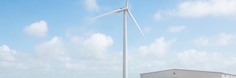 Medium wind turbine beside a Florida citrus packing house under a bright coastal sky